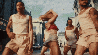a group of men and a woman are dancing on a street in front of a building that has the word gardiner on it