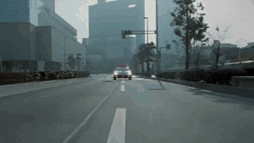 a police car is driving down a city street with buildings in the background