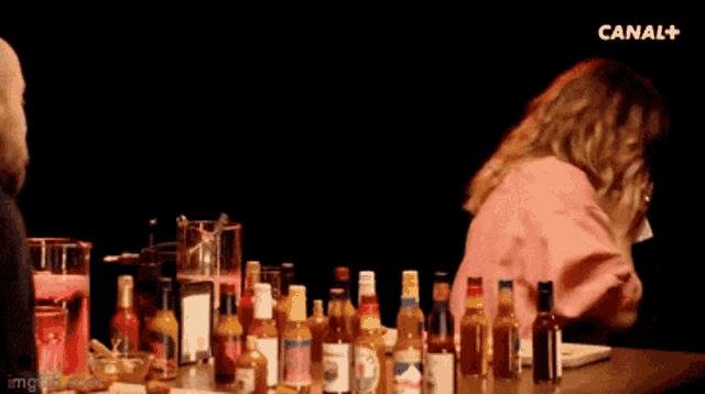 a woman sits at a table with bottles of alcohol and the word hyper bien written on the screen