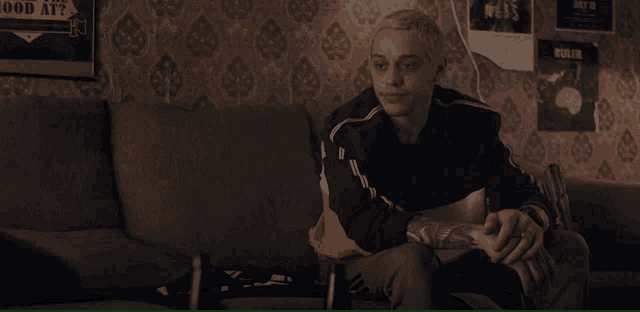 a man sits on a couch in front of a wall with a poster that says good at