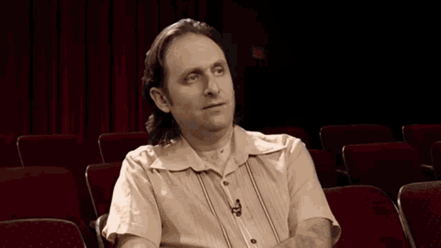 a man is sitting in a theater making a hand gesture with his hands .
