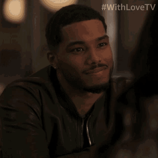 a man in a leather jacket is smiling while sitting at a table with #withlovetv written on the bottom