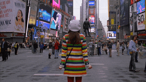 a woman in a rainbow colored sweater stands in front of a sign that says mamma mia
