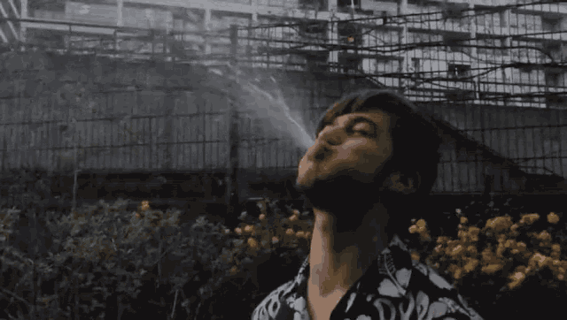a man with a beard is blowing smoke out of his mouth in front of a building