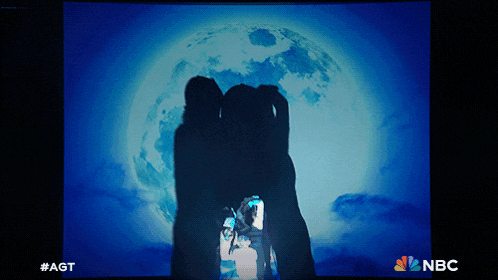 a screen shows a silhouette of two people in front of a full moon and says #agt on the bottom