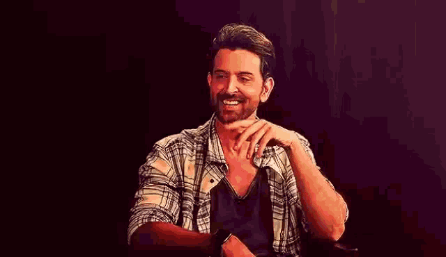 a man with a beard is sitting in a chair with his hand on his chin .