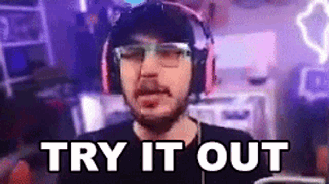 a man wearing headphones and glasses is saying `` try it out '' in a video game room .