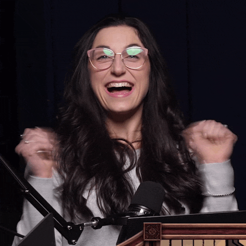 a woman wearing glasses is standing in front of a microphone with her arms in the air