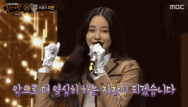 a girl in a school uniform is singing into a microphone with a mbc logo behind her