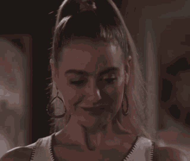 a woman wearing hoop earrings and a white tank top smiles
