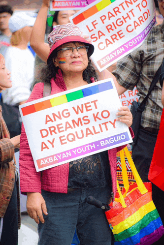 a woman in a pink jacket holds a sign that says ang wet dreams ko ay equality