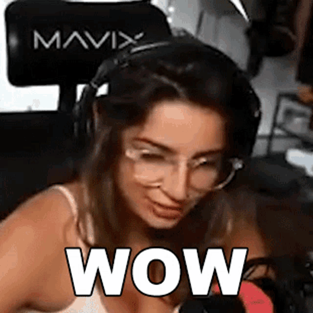 a woman wearing headphones and glasses is sitting in front of a microphone with the word wow written on her face .