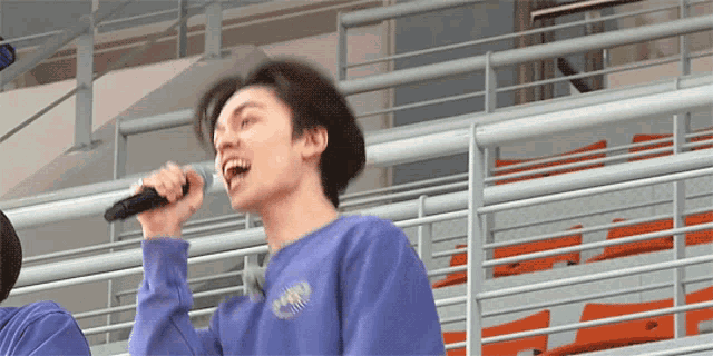 a young man singing into a microphone while wearing a purple sweatshirt that says ' cnn ' on it