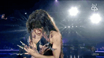 a woman with long nails is on a stage with the number 20j on the bottom right