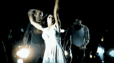 a woman in a white dress is dancing in the dark with a group of people behind her .