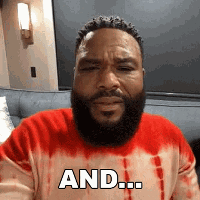 a man with a beard wearing a red tie dye sweater is sitting on a couch and saying and ...