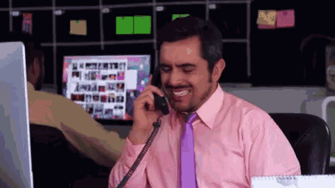 a man in a pink shirt and purple tie is smiling while talking on a phone