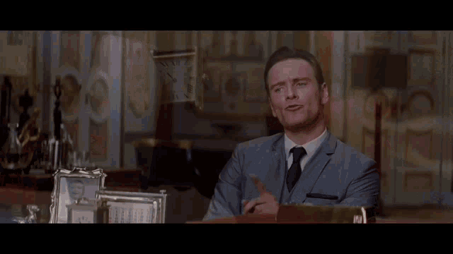 a man in a suit and tie is talking to another man in a dark room .