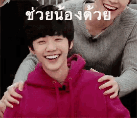 a boy in a pink hoodie is being hugged by a man in a grey sweater .