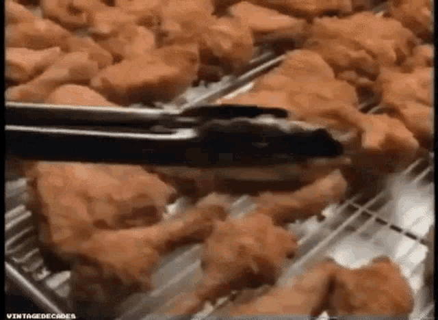 a person is using tongs to pick up fried chicken from a tray .