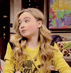 a young girl wearing a yellow shirt is sitting on a couch .