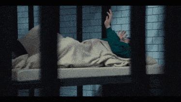 a man in a green shirt is laying on a bed with a white blanket