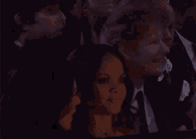 a group of people are sitting in a dark room and one of them is drinking from a glass .