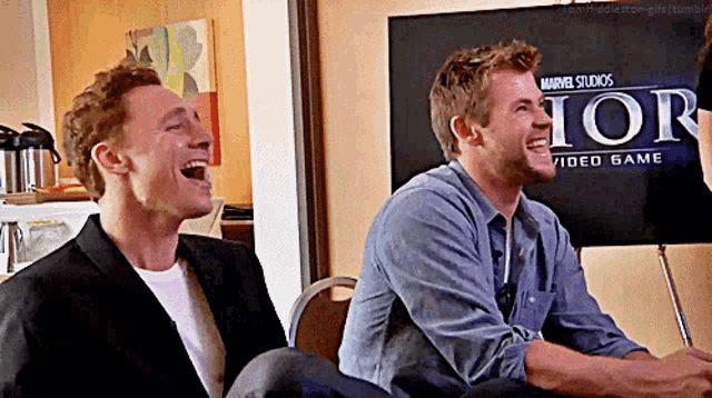 two men are laughing in front of a sign that says ior video game .