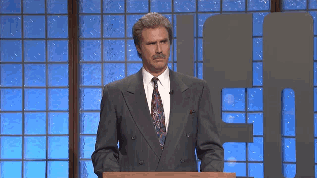 a man in a suit and tie stands at a podium in front of a glass wall with the letter f on it