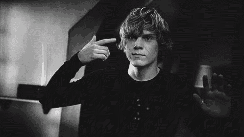 a man in a black shirt is pointing his finger at his head .