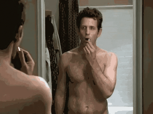 a shirtless man is brushing his teeth in front of a mirror in the bathroom .
