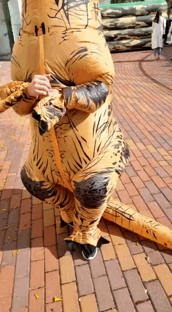 a person in an inflatable t-rex costume is standing on a brick sidewalk .