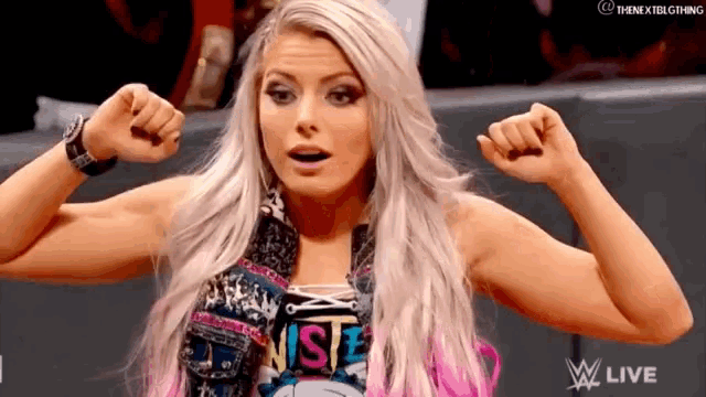 a woman is flexing her muscles in front of a crowd while wearing a wrestling outfit .