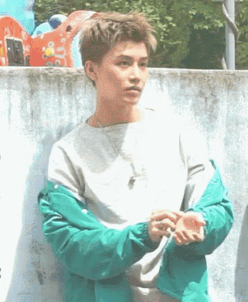 a young man wearing a green jacket and a white sweater is standing in front of a wall .