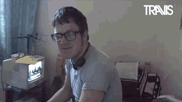 a man wearing glasses and headphones is sitting in front of a television with the word travis on the bottom