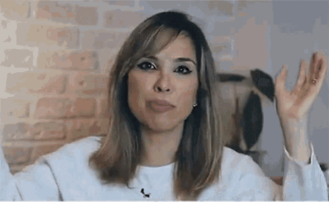 a woman in a white shirt is making a funny face with her hands up .