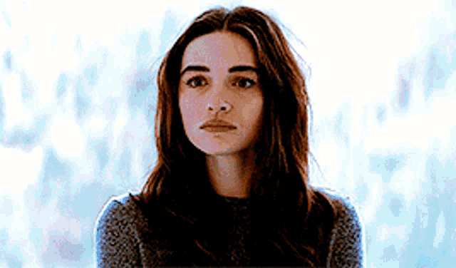 a woman with long hair is wearing a sweater and looking at the camera with a serious look on her face .