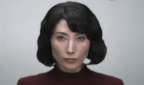 a woman in a red sweater is looking at the camera with a serious look on her face .