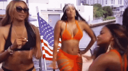 three women in bikinis are standing next to an american flag .