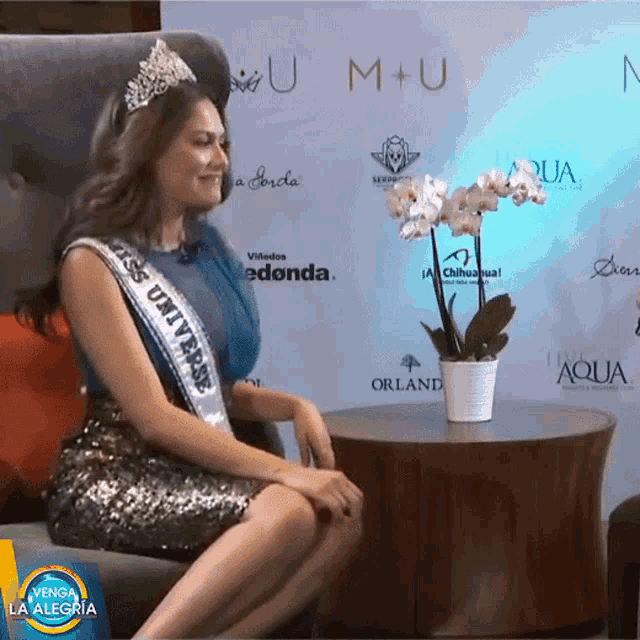 a woman wearing a sash that says miss universe sits on a chair