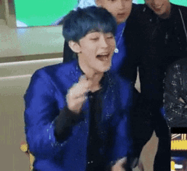 a man with blue hair is laughing while wearing a blue jacket and a black shirt .