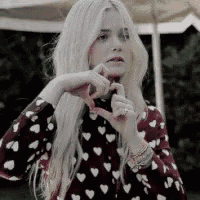 a woman is making a heart shape with her hands while wearing a heart printed shirt .
