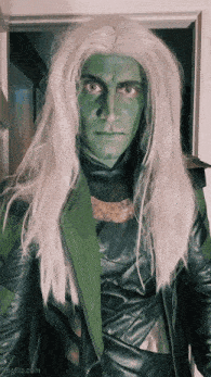 a man with green paint on his face and long white hair is standing in a doorway
