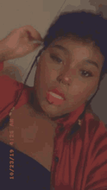a woman in a red shirt and black top is taking a selfie with her mouth open .