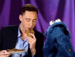 a man is eating a cookie while a cookie monster looks on