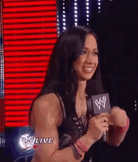 a woman is holding a microphone and smiling while standing in front of a red background .