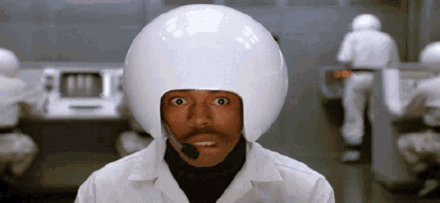 a man wearing a white helmet and a microphone looks at the camera