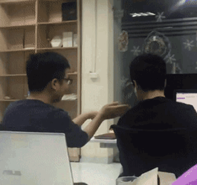 two men sitting at a desk with a laptop that says asus on it