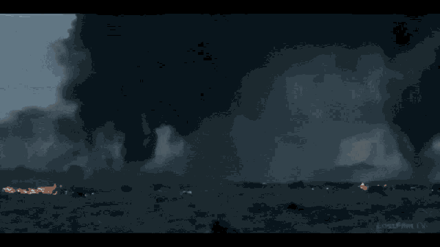 a man in a suit is walking through a foggy field with a cross behind him