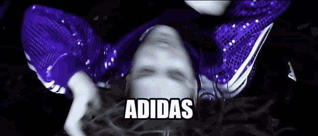 a woman in a purple sequined top is laying on her back with the word adidas written above her